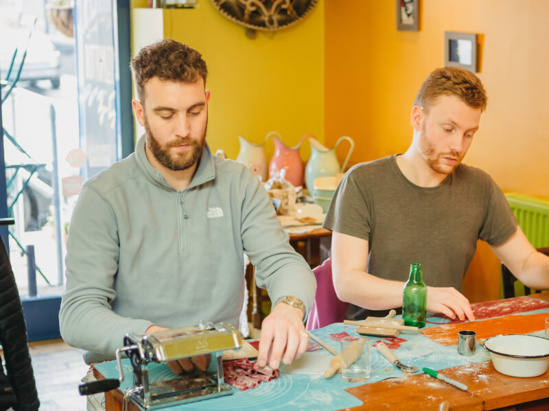 Two men learn how to make pasta at a date night.